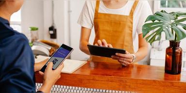 Café employee using a tablet while a customer completes a mobile payment, used as illustrative payment-resilience imagery.