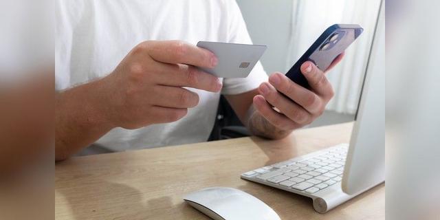 Person holding a smartphone and card for an online transaction at a desk