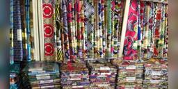 Colourful textile rolls stacked and hanging at a Nigerian fabric market stall.
