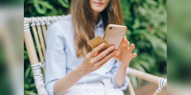 Woman holding a smartphone and card while making an online purchase outdoors