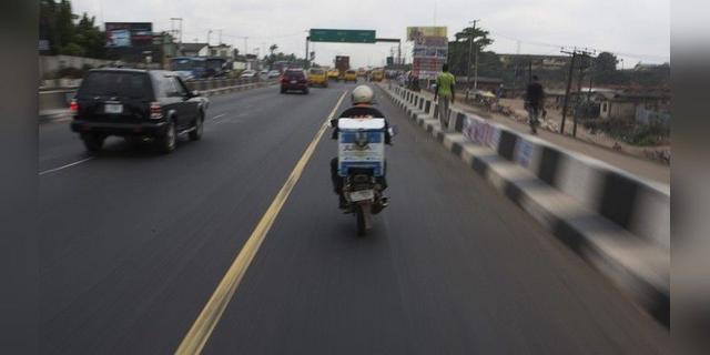 A delivery rider carrying a parcel rides on a busy Lagos highway.