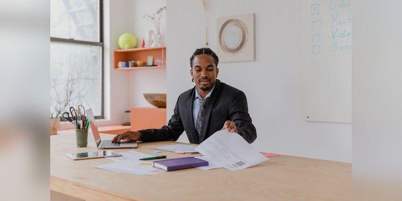 Business professional organising documents beside a laptop at a modern desk, used as illustrative business-operations imagery