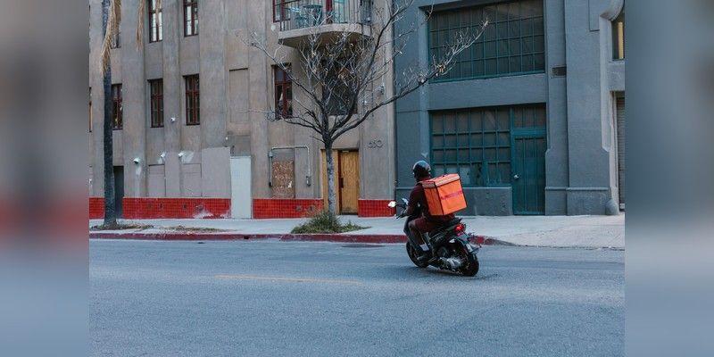 Courier riding a motorcycle with a delivery bag in an urban street, used as illustrative delivery imagery.