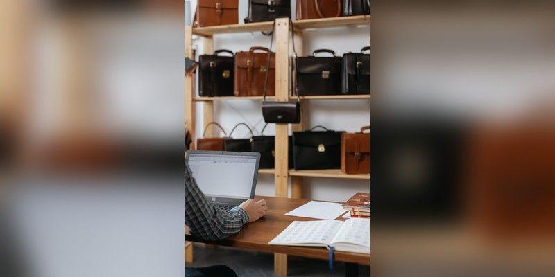 Shop owner working on a laptop at a retail desk with bags on shelves, used as illustrative small-business imagery