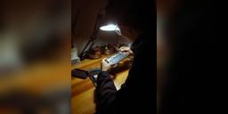Technician repairing a smartphone under a desk lamp at a workbench