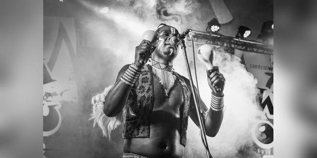 Musician singing and holding maracas on stage, used as illustrative live-music imagery.