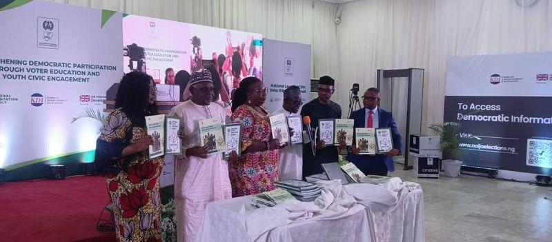 INEC officials unveiling voter education manuals at an event in Abuja with stakeholders and youth representatives present.