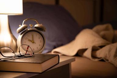 Peaceful bedroom with soft lighting, a book on a bedside table and a person preparing for a restful night's sleep.