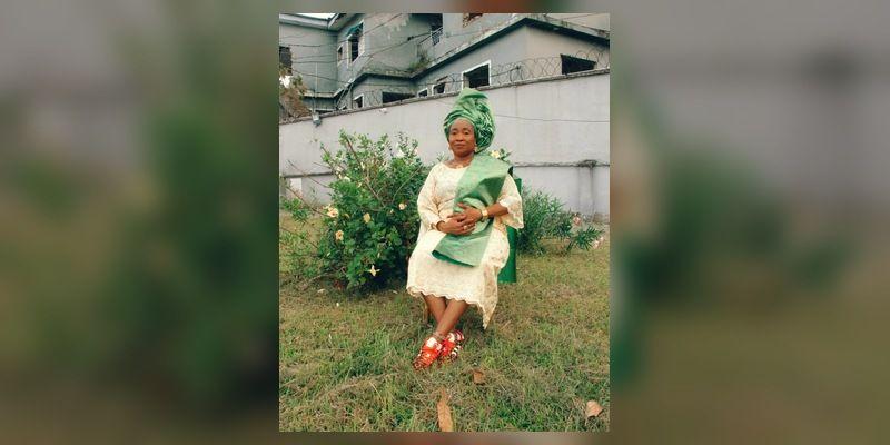 A woman wearing coordinated green-and-cream Àṣọ Ẹbí style clothing and colourful adidas sneakers at an outdoor celebration setting.