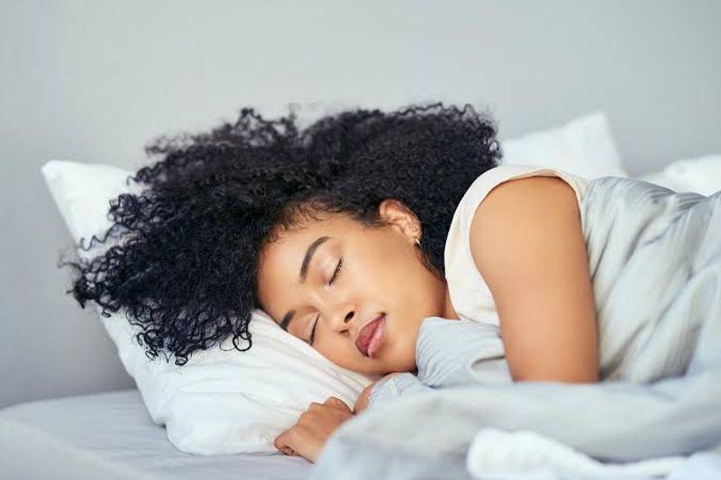 A person sleeping peacefully in a dark, comfortable bedroom with soft lighting and a bedside clock.