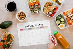 Weekly meal plan with healthy ingredients, fresh vegetables, shopping list and meal prep containers on a kitchen counter.