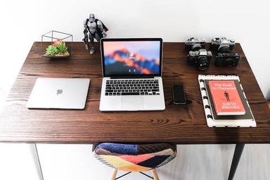 Organised office desk with a laptop, notebook, cable organiser, desk lamp and neatly arranged stationery.
