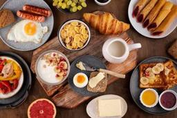 Healthy breakfast spread featuring oatmeal, fruit smoothie, avocado toast, boiled eggs, yoghurt and fresh fruits on a kitchen table.