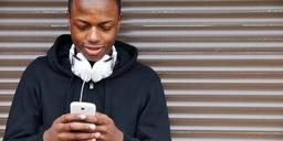 A young Nigerian smartphone user looks at a handset while wearing white headphones.