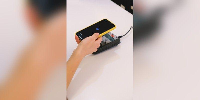 Hand holding a smartphone over a contactless payment terminal, used as illustrative digital-payments imagery.