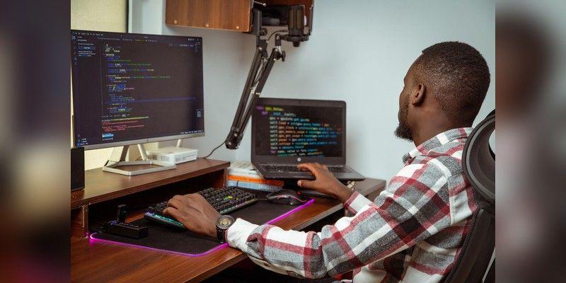 Developer working on a desktop and laptop in an office, used as illustrative app-development imagery.