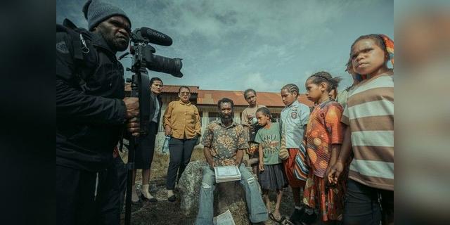 Filmmaker holding a video camera beside people gathered outdoors, used as illustrative documentary-production imagery.