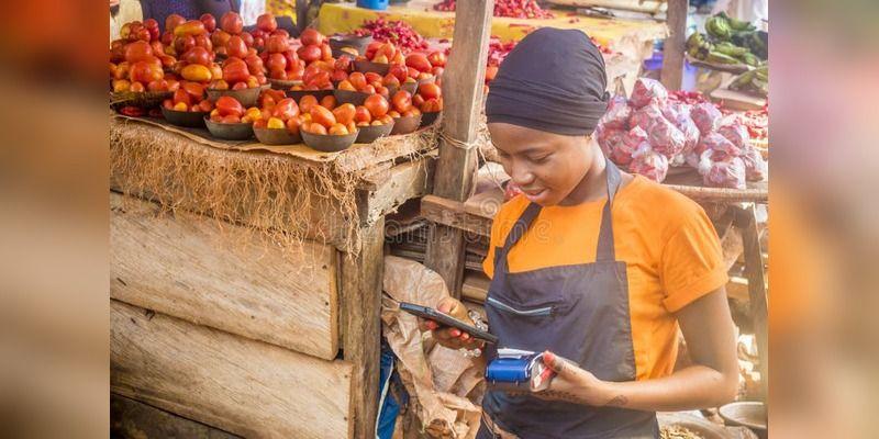 A Nigerian market seller using a payment terminal at a shop counter.