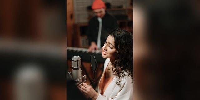 Singer using a studio microphone while a musician plays keyboard, used as illustrative music-production imagery.