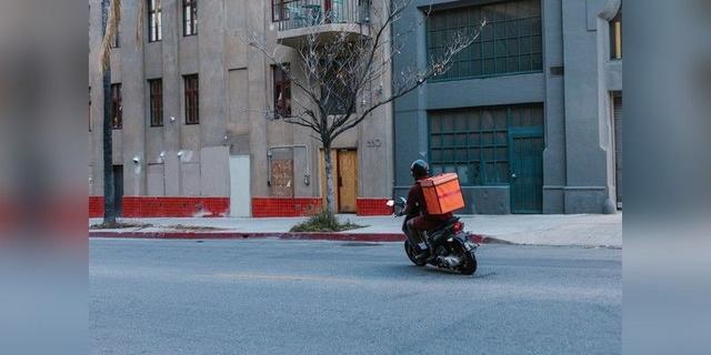 Courier riding a motorcycle with a delivery bag in an urban street, used as illustrative delivery imagery.