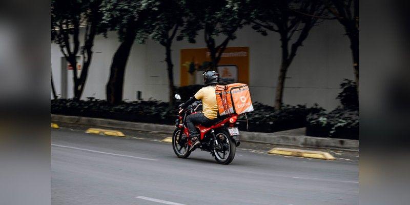 Delivery rider on a motorcycle with an insulated bag on an urban street, used as illustrative delivery imagery