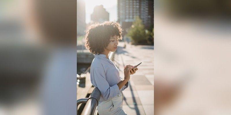 Woman checking a smartphone beside a railing outdoors, used as illustrative mobile-access imagery.