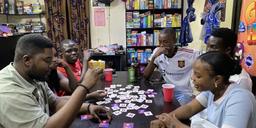 Six people play a tabletop word game at a table surrounded by board games in Nigeria.