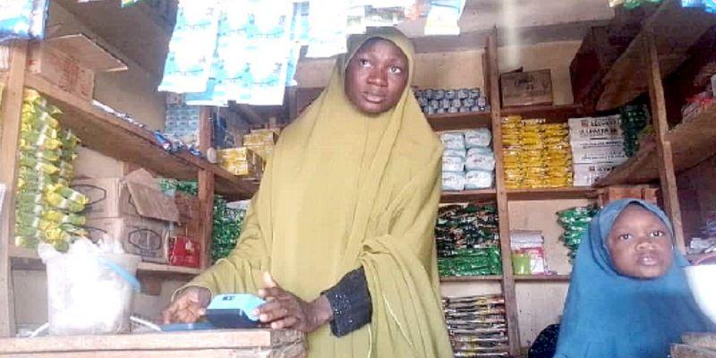 A Nigerian trader uses a blue POS device inside a small provision shop.