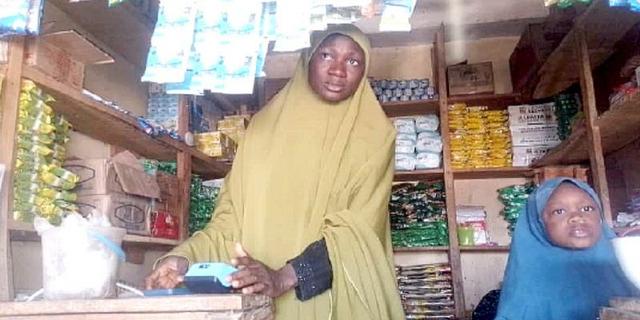 A Nigerian trader uses a blue POS device inside a small provision shop.